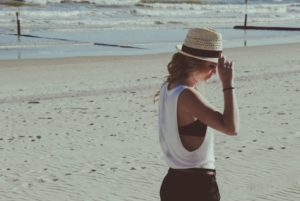 Dame på stranda med hatt og sommerhår.